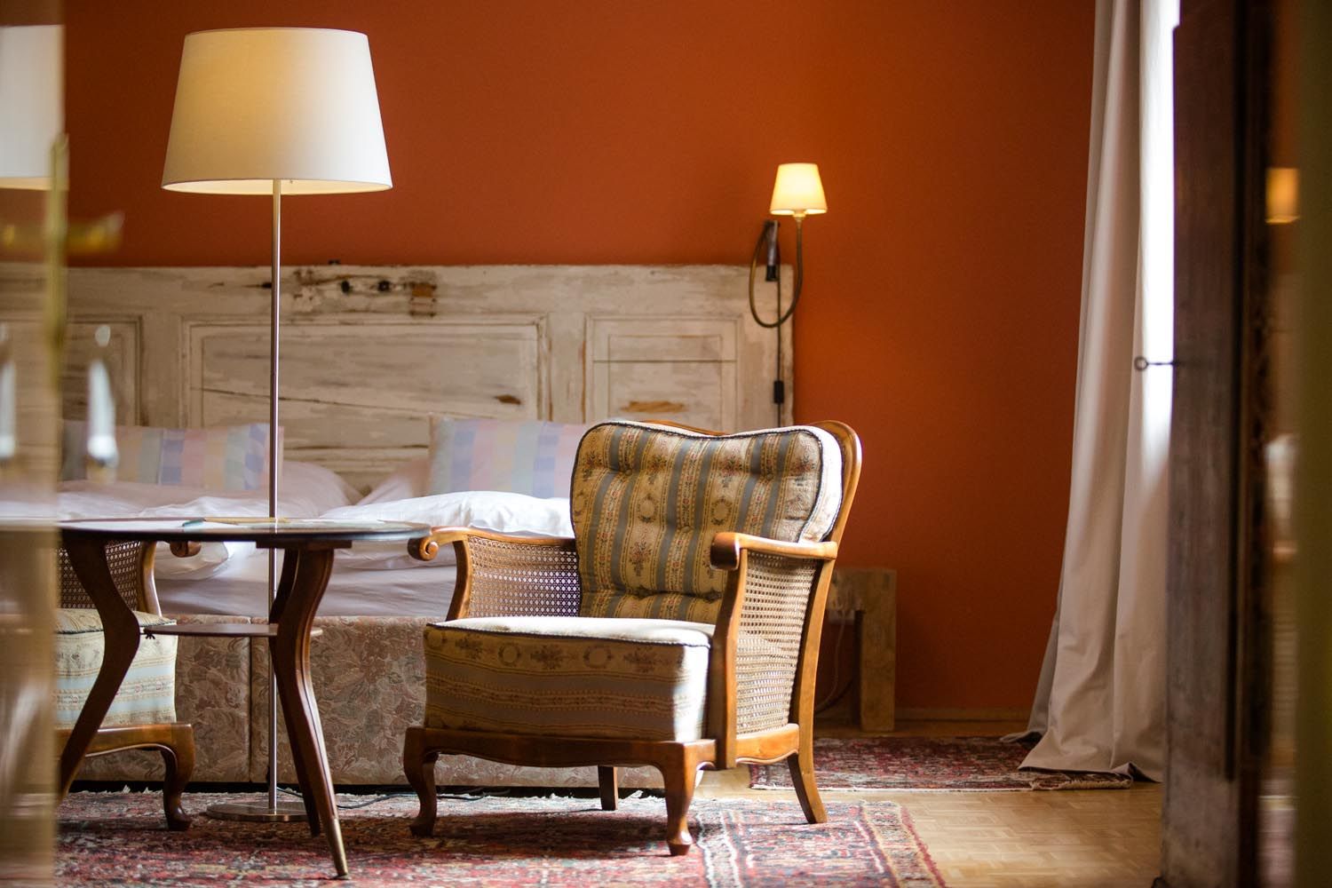 Gemütliches Zimmer mit Sessel, Tisch und Stehlampe vor einem Bett mit rustikaler Holzverkleidung.