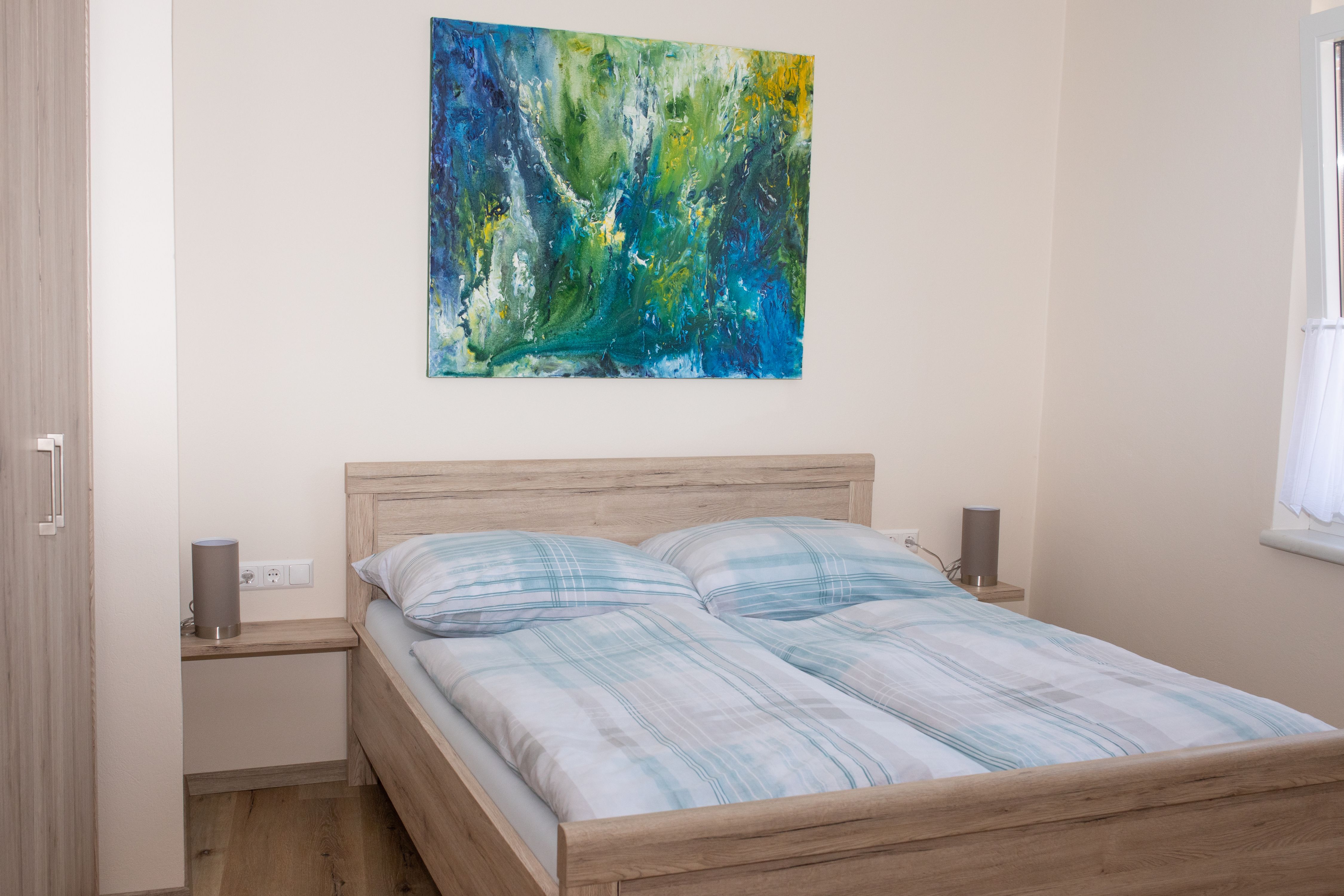 Schlafzimmer mit Doppelbett, abstraktem Gemälde an der Wand und Fenster mit Vorhang.