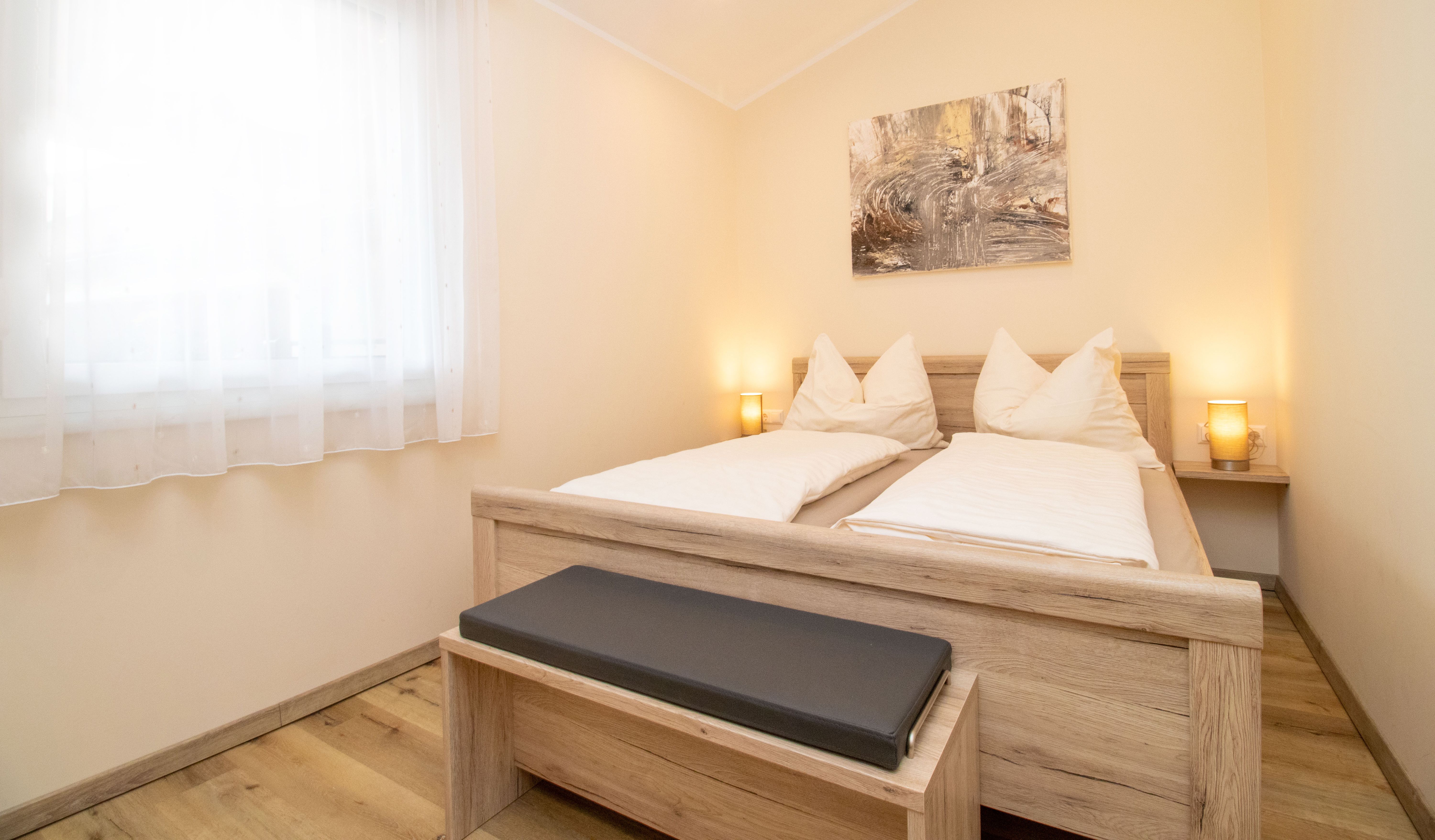 Ein gemütliches Schlafzimmer mit einem Doppelbett aus Holz, zwei Nachttischlampen und einem Bild an der Wand.