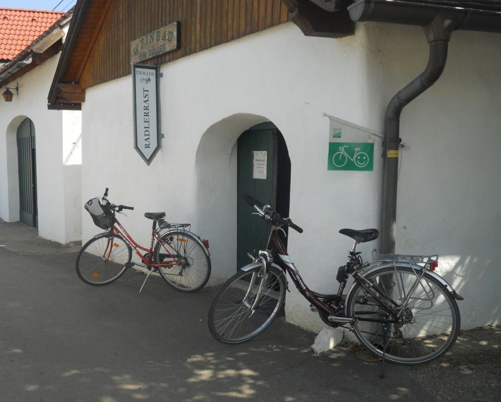 Zwei Fahrräder vor einem Gebäude mit der Aufschrift 'Weinbau Radlerrast'.