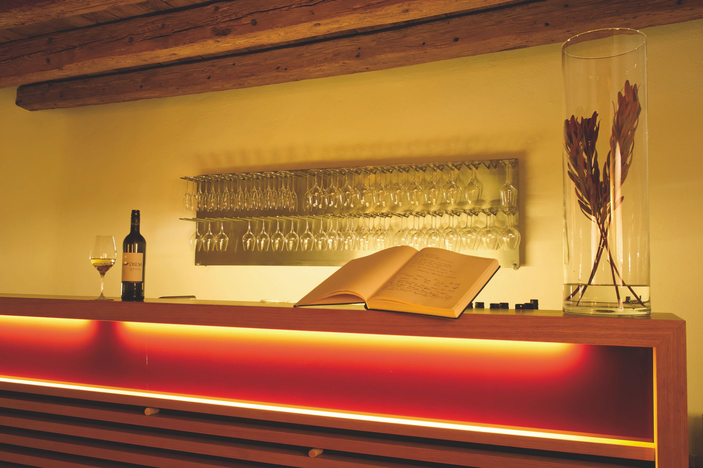 Wine tasting room with illuminated bar, wine glasses, a wine bottle and an open guest book.