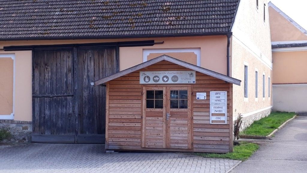 Malý dřevěný obchod před velkou budovou s dřevěnou bránou.
