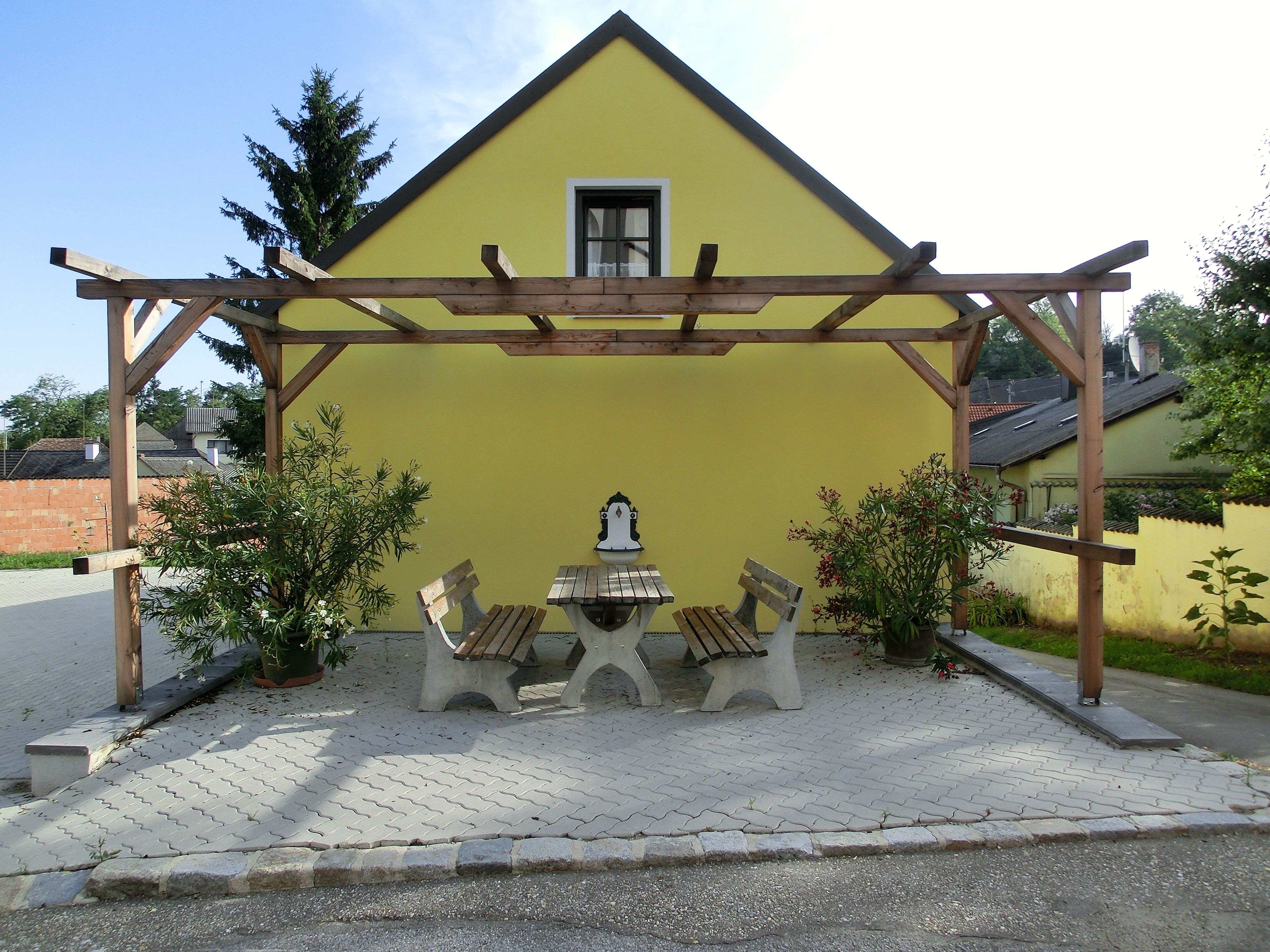 Gelbes Gebäude mit Pergola und Sitzbereich im Freien.