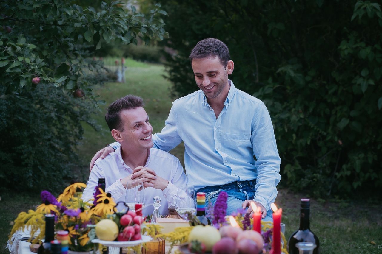 Two men sit at a table outside, surrounded by flowers and candles.