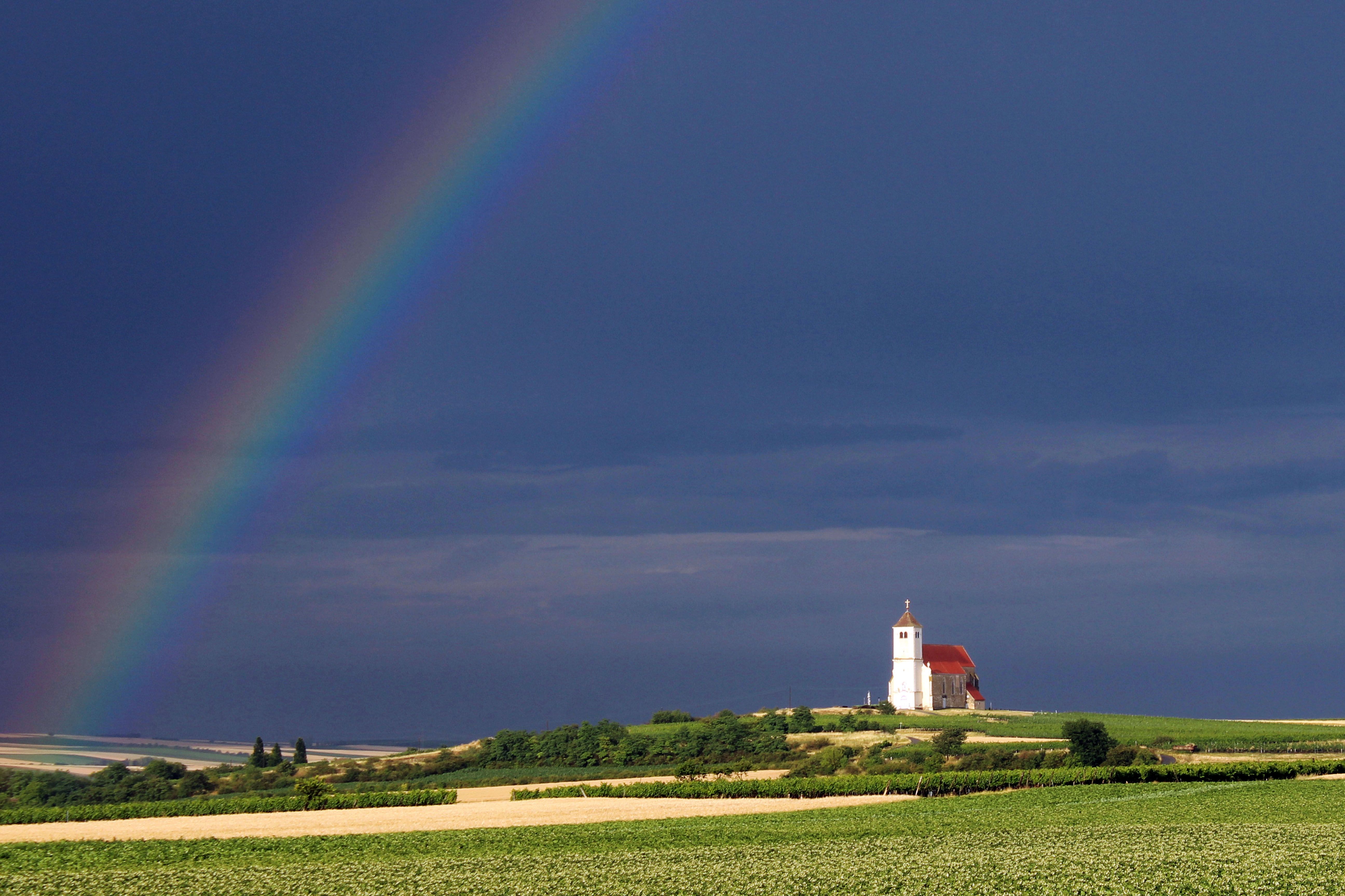 Eine Kirche auf einem Hügel unter einem dunklen Himmel mit einem Regenbogen.