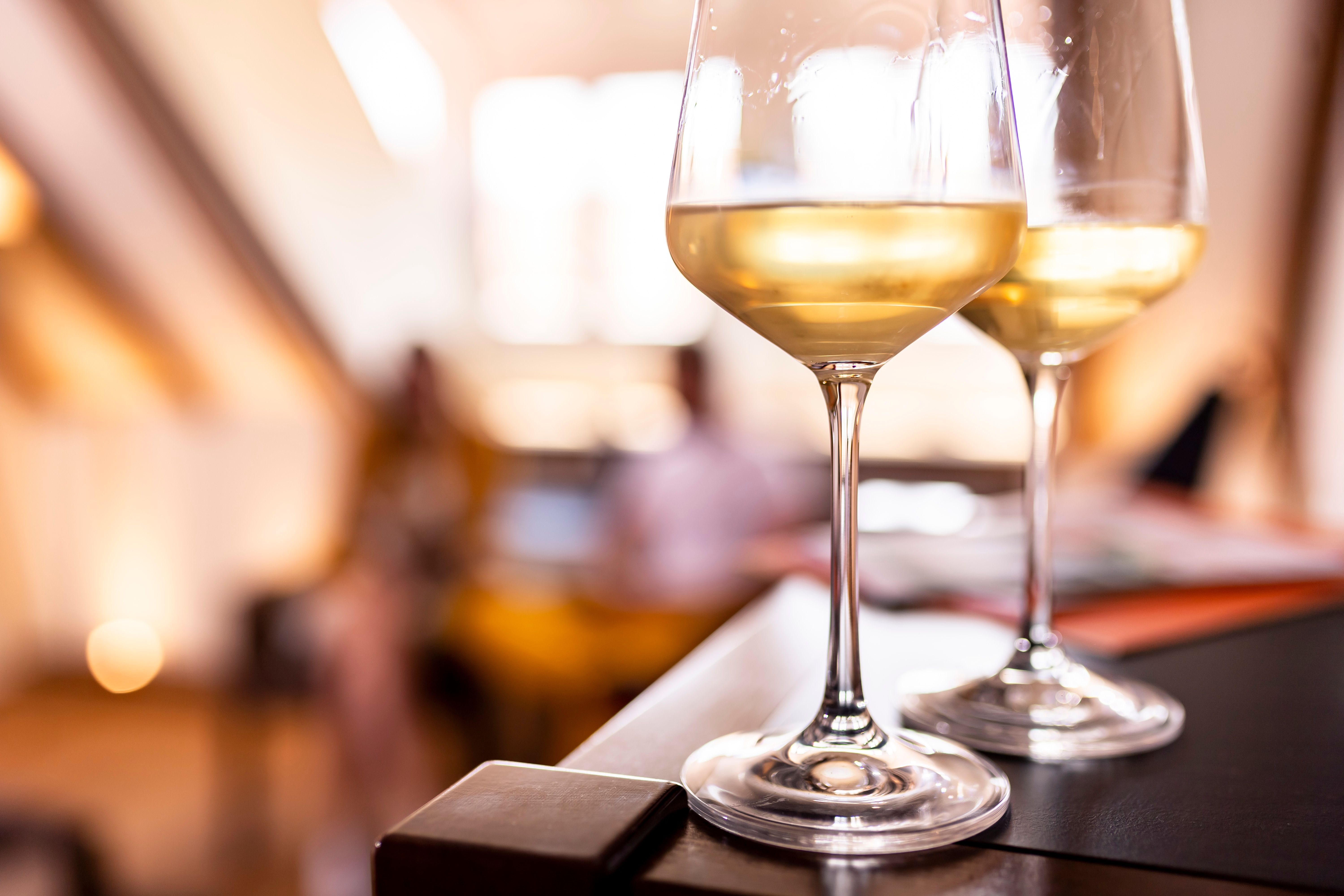 Zwei Weingläser mit Weißwein auf einem Tisch, unscharfer Hintergrund.