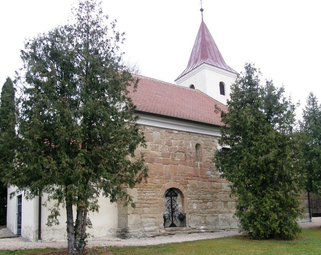 Eine alte Kirche mit einem roten Ziegeldach und einem Turm, umgeben von Bäumen.