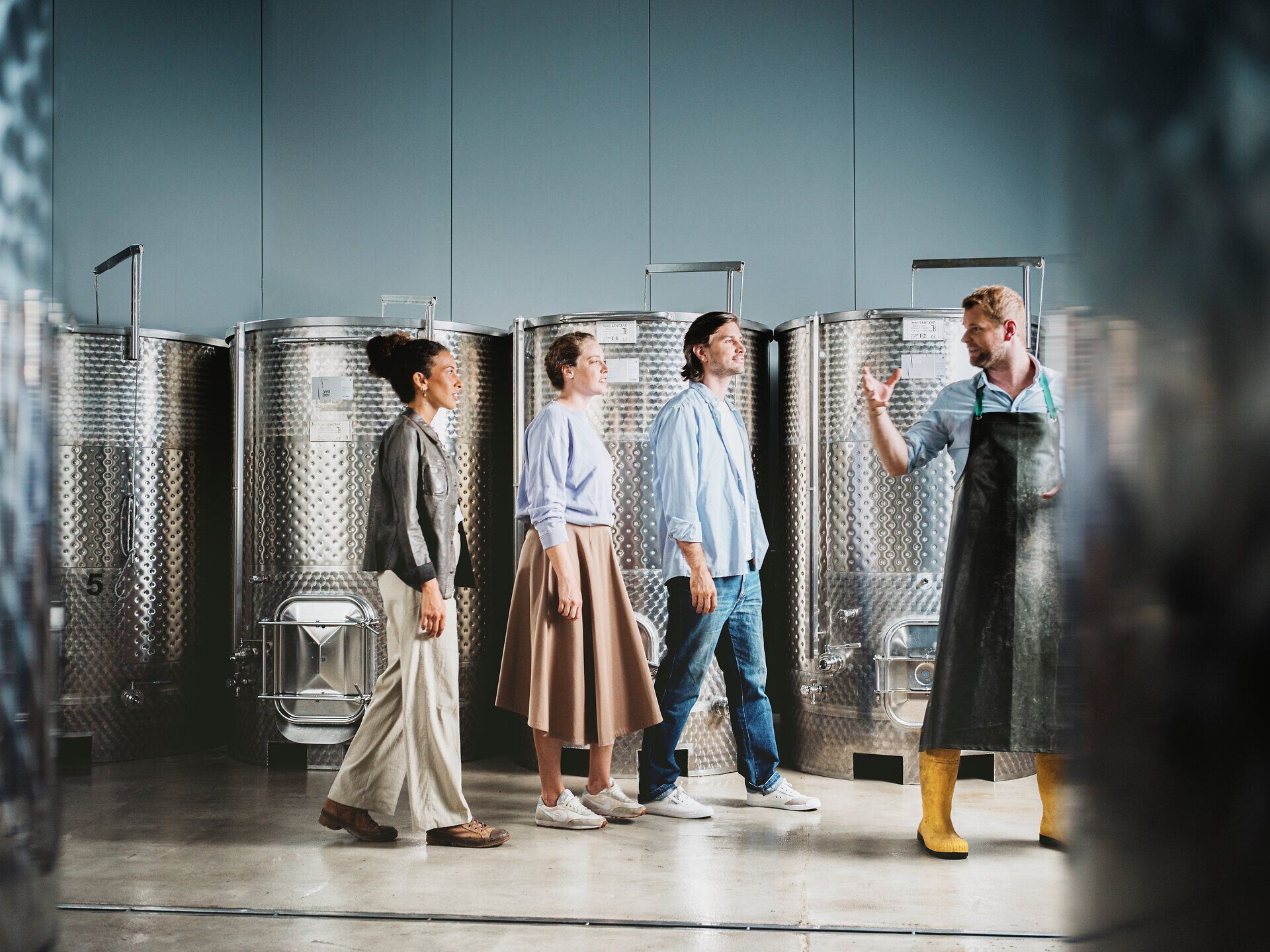 Eine Gruppe von Menschen schlendert durch die beeindruckenden Weinreben, umgeben von der malerischen Landschaft des Weinviertels. Die warme Herbstsonne taucht die Szenerie in goldenes Licht und verspricht genussvolle Erlebnisse bei der Weinernte.