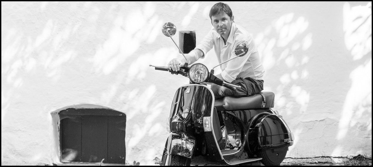 Person auf einer Vespa vor einer weißen Wand.