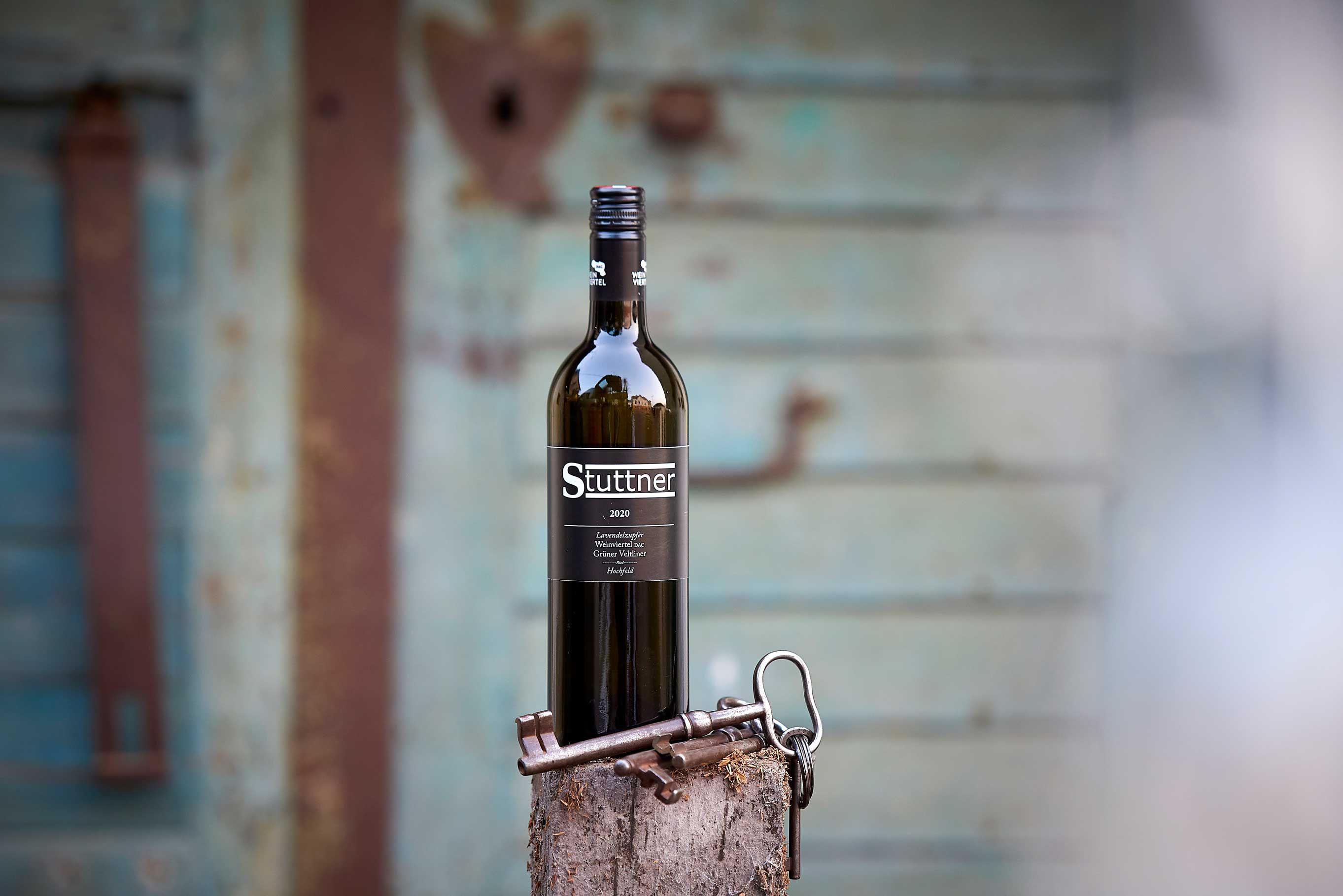 A Stuttner wine bottle stands on a tree stump with old keys in front of a blurred, rustic background.