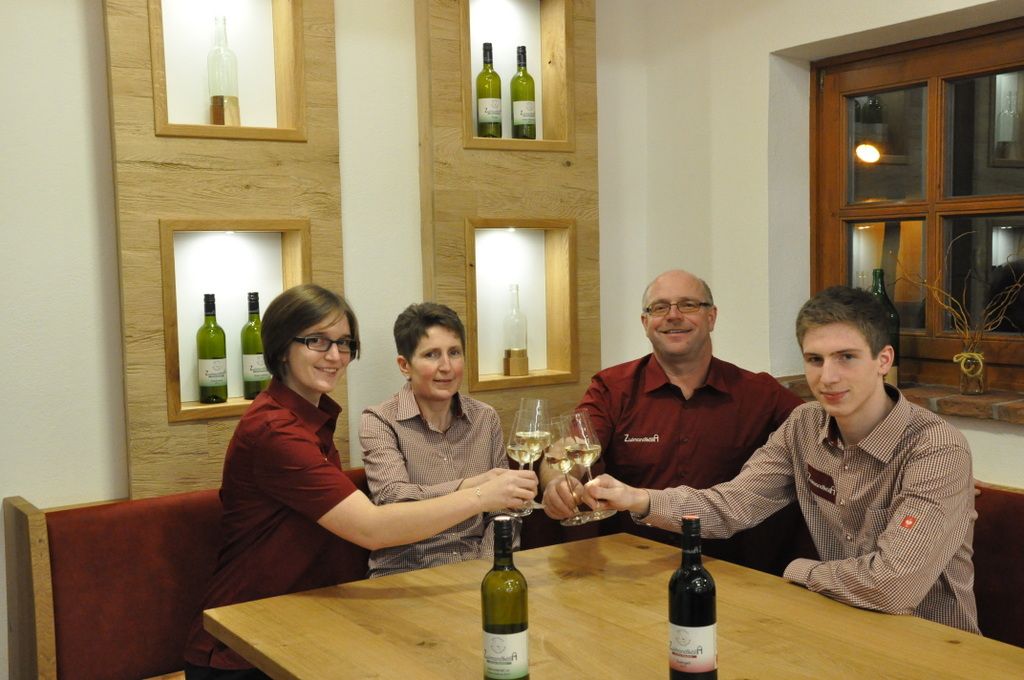 Vier Personen stoßen mit Weingläsern an einem Tisch an.