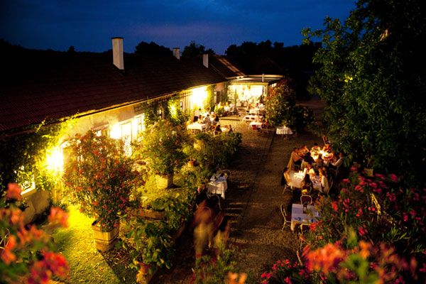 Abendliche Gartenterrasse mit beleuchteten Tischen und Pflanzen.