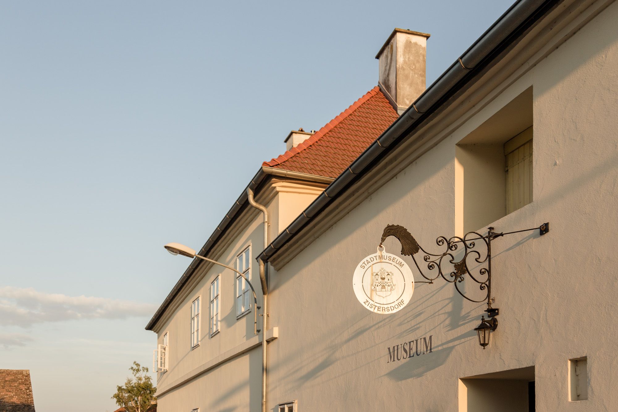 Außenansicht des Stadtmuseums Zistersdorf mit einem dekorativen Schild und einem Laternenpfahl im Vordergrund.