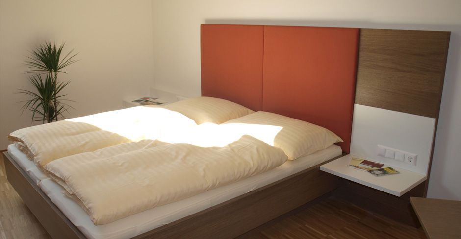 Modernes Gästezimmer mit Doppelbett, rotem Kopfteil und Pflanzen.