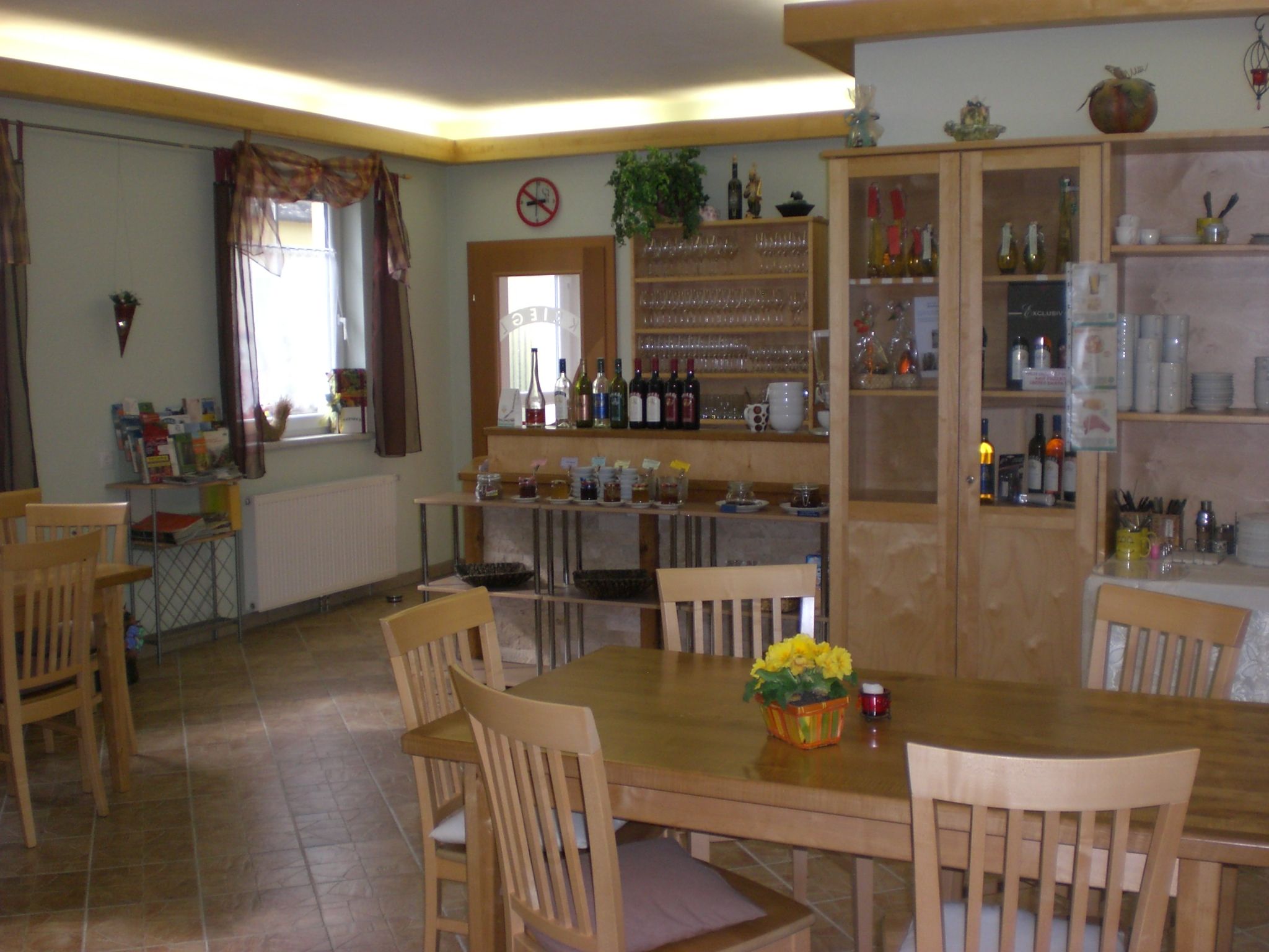 Ein gemütlicher Verkostungs- und Frühstücksraum mit Holzmöbeln, Regalen mit Gläsern und Flaschen, und einem Tisch mit Blumen.