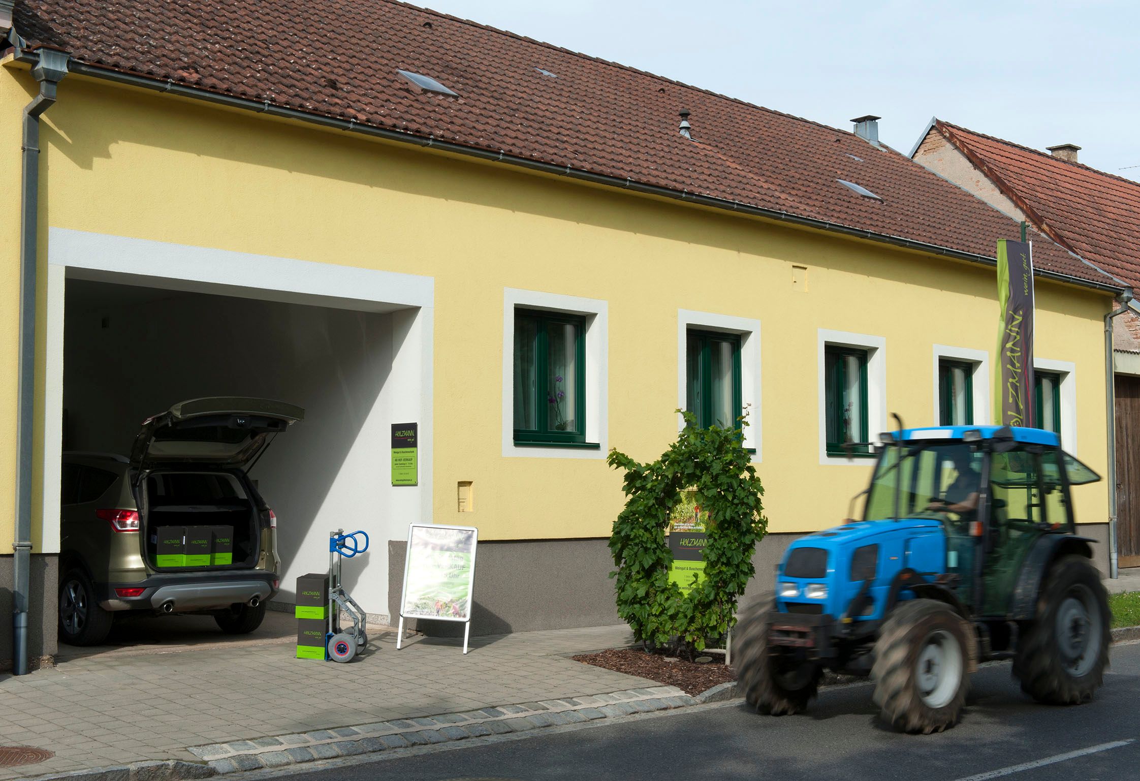 Yellow building with open garage, car and tractor in front of it.
