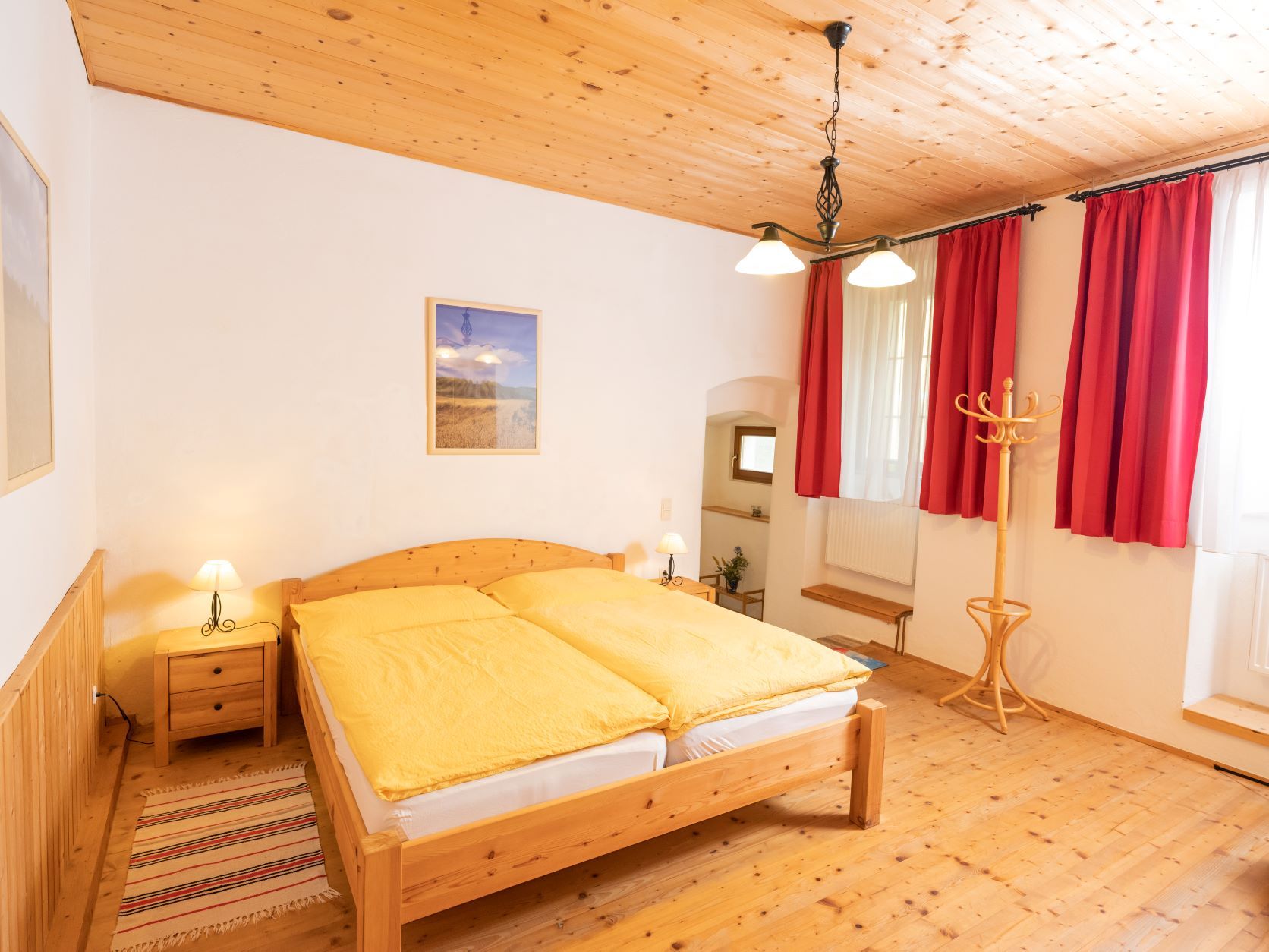 Cozy bedroom with wooden furniture, yellow bed linen and red curtains.