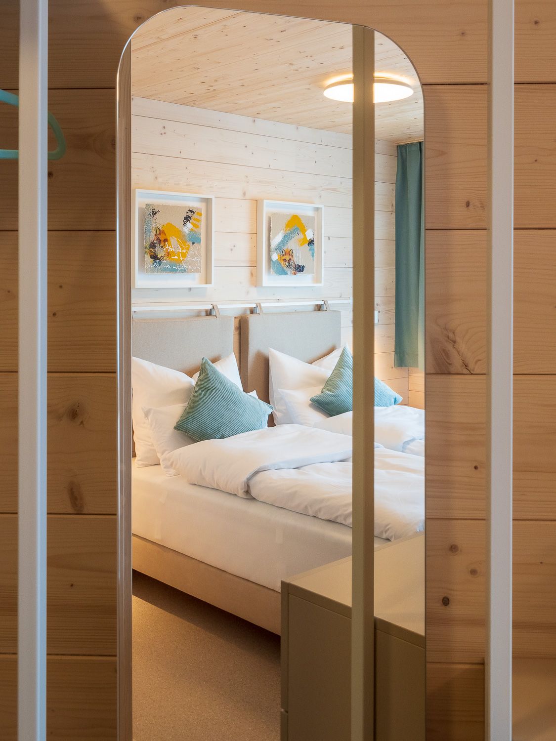 Ein gemütliches Doppelzimmer mit Holzverkleidung, zwei Betten, blauen Kissen und moderner Kunst an der Wand.
