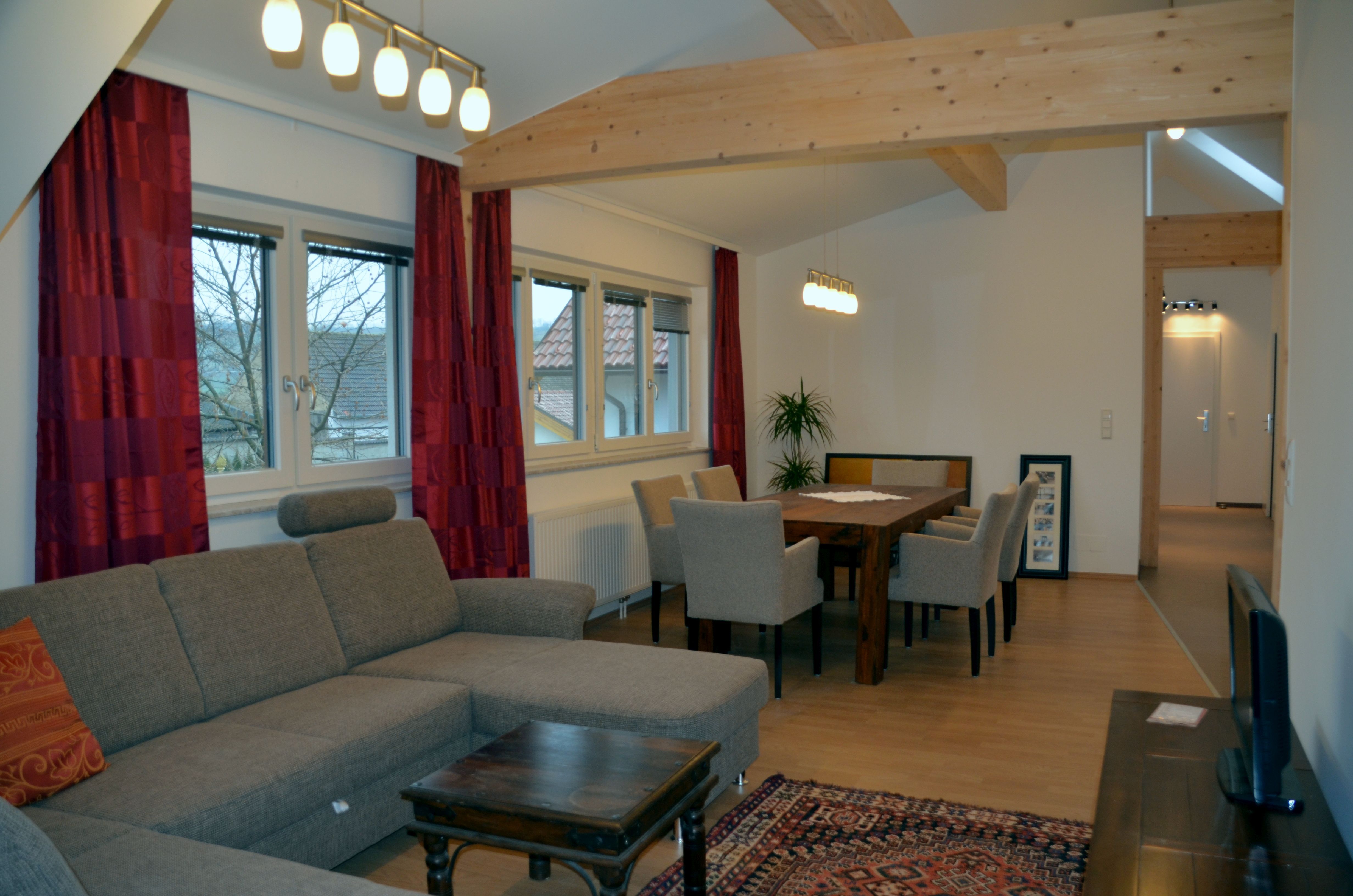 Living room with gray sofa, wooden table and chairs, red curtains and ceiling lights.