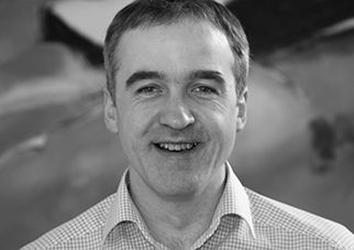 Black and white photo of a smiling man in a plaid shirt.