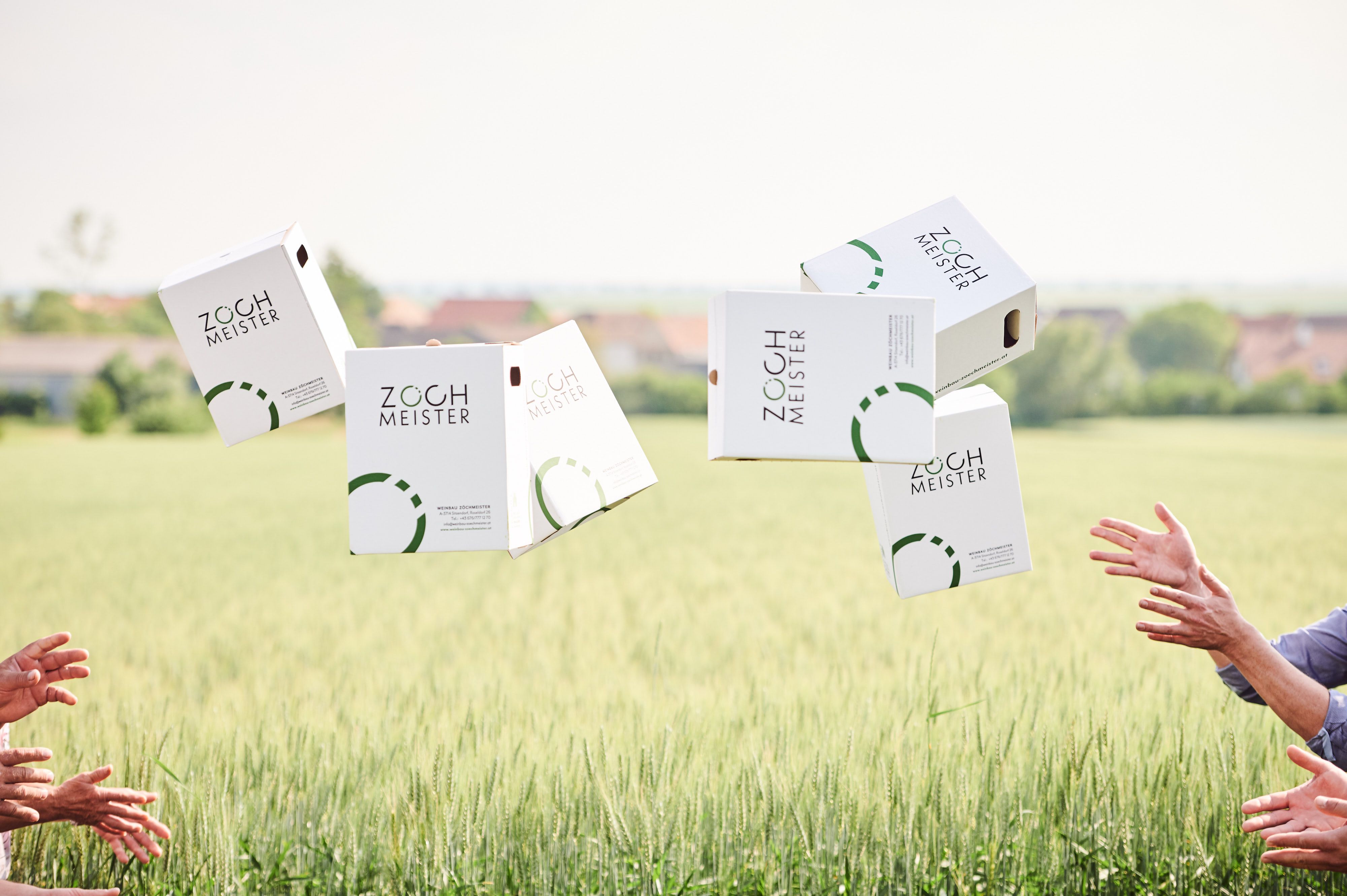 Zöchmeister wine cartons fly across a field, hands catch them.