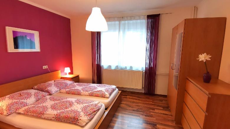 Gemütliches Schlafzimmer mit Doppelbett, pinker Wand und Holzmöbeln.