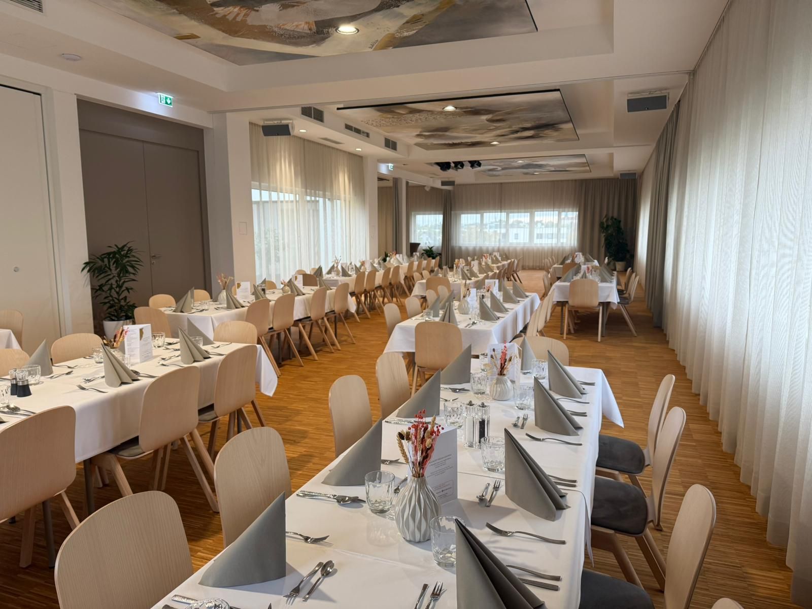 Ein elegant gedeckter Veranstaltungssaal mit langen Tischen, weißen Tischdecken und gefalteten Servietten.