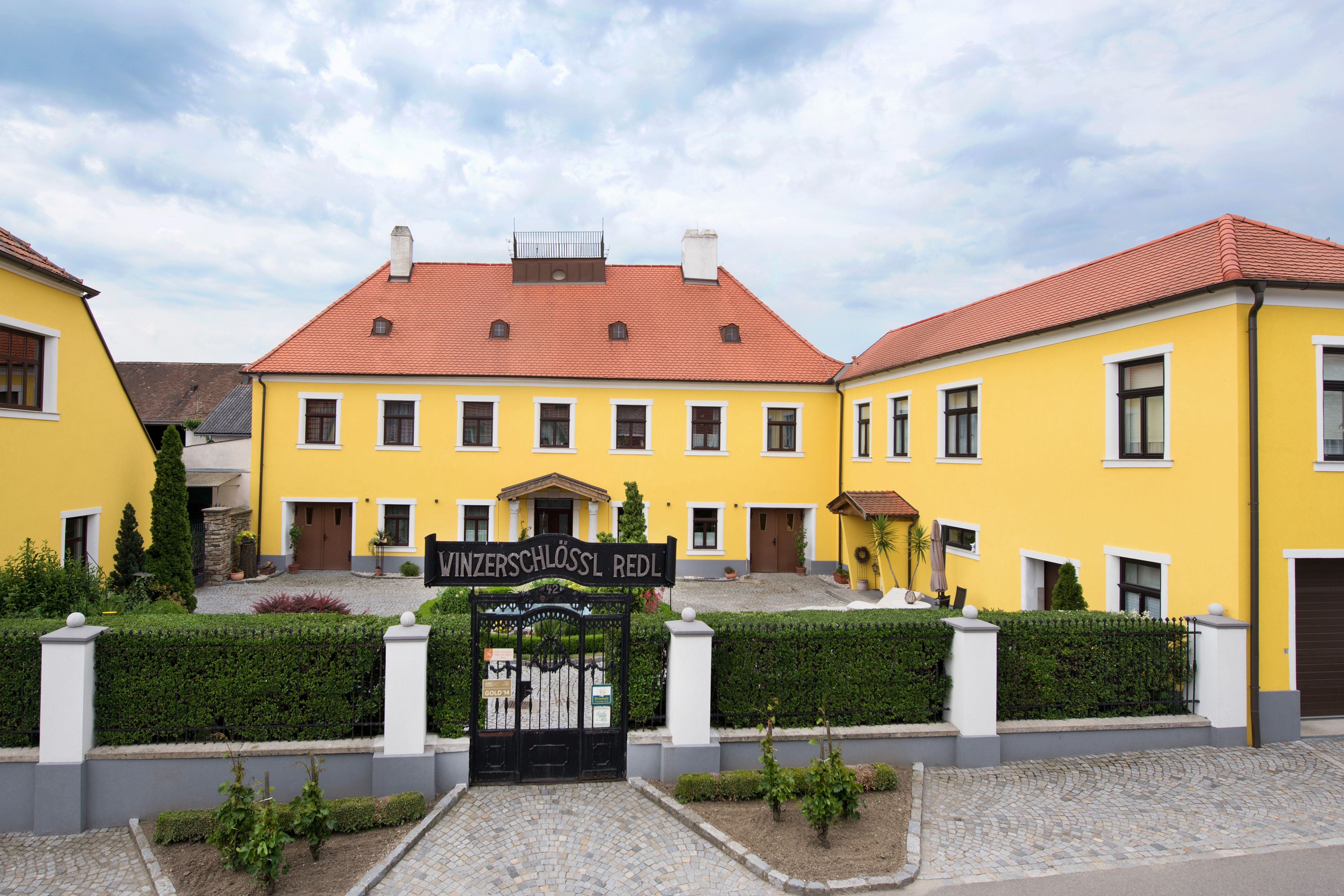 Gelbes Gebäude mit rotem Dach und Tor mit der Aufschrift 'Winzerschlössl Redl'.