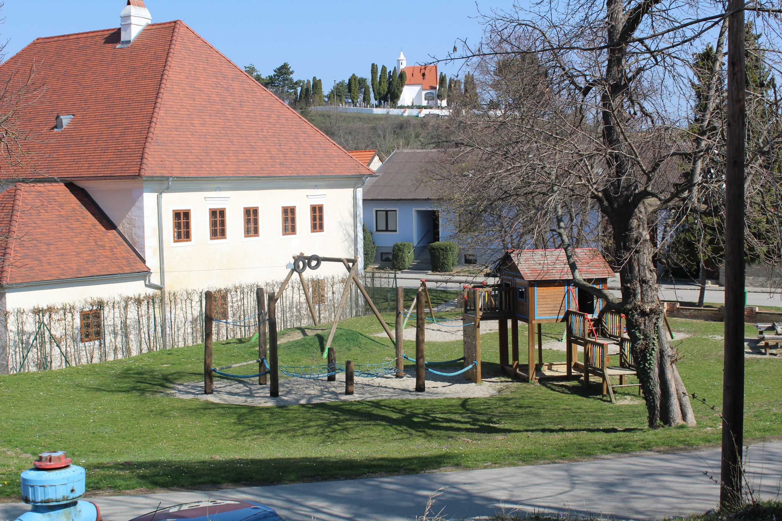 Ein Kinderspielplatz mit Klettergerüst und Schaukel neben einem Gebäude mit rotem Dach.