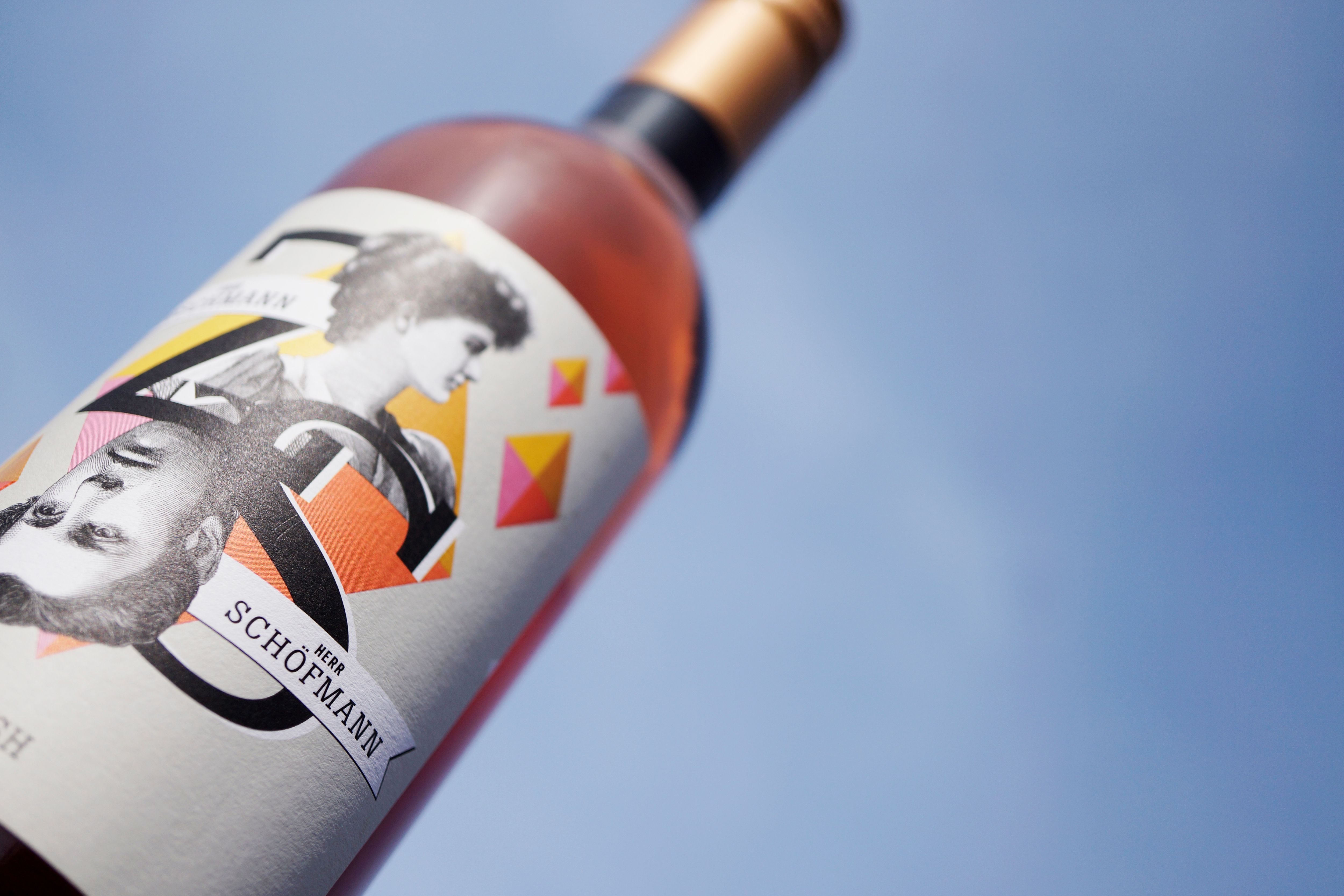 Nahaufnahme einer Weinflasche mit künstlerischem Etikett vor blauem Himmel.