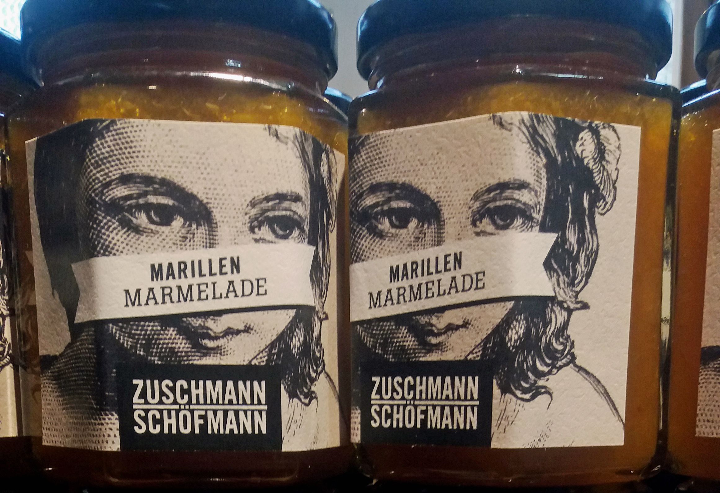 Zwei Gläser Marillenmarmelade mit Etiketten, die ein Gesicht zeigen.
