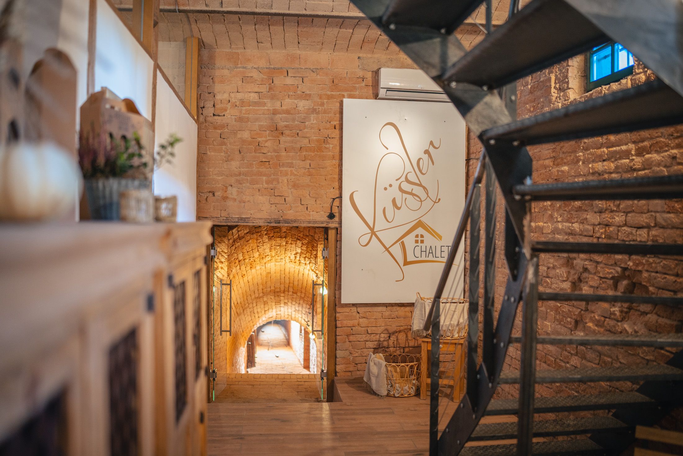 Innenraum im Winzerhof Küssler mit Backsteinwänden, schwarzer Treppe und beleuchtetem Gewölbegang.
