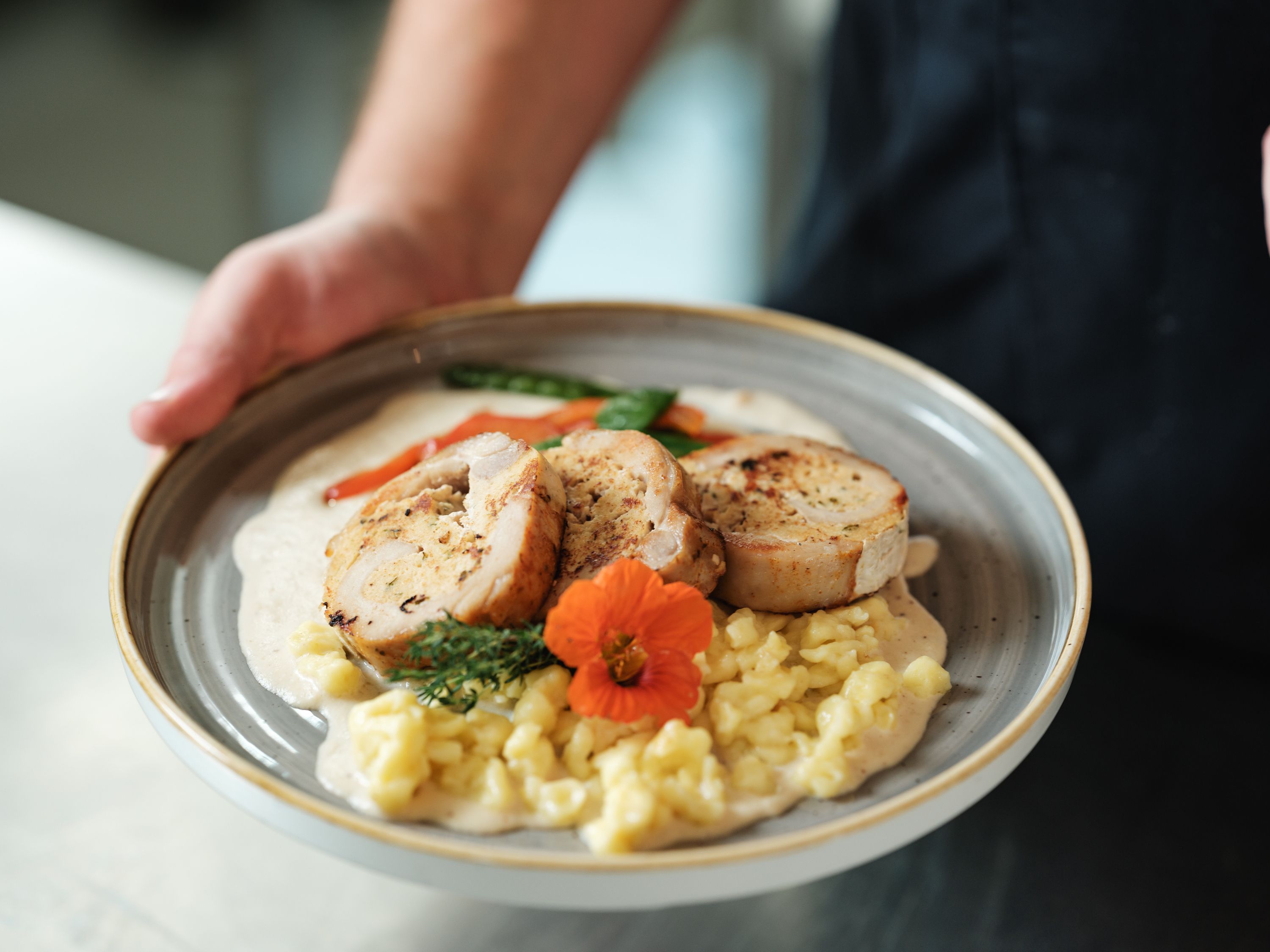 Ein Teller mit gefülltem Fleisch, Spätzle, Gemüse und einer Blume als Garnitur.
