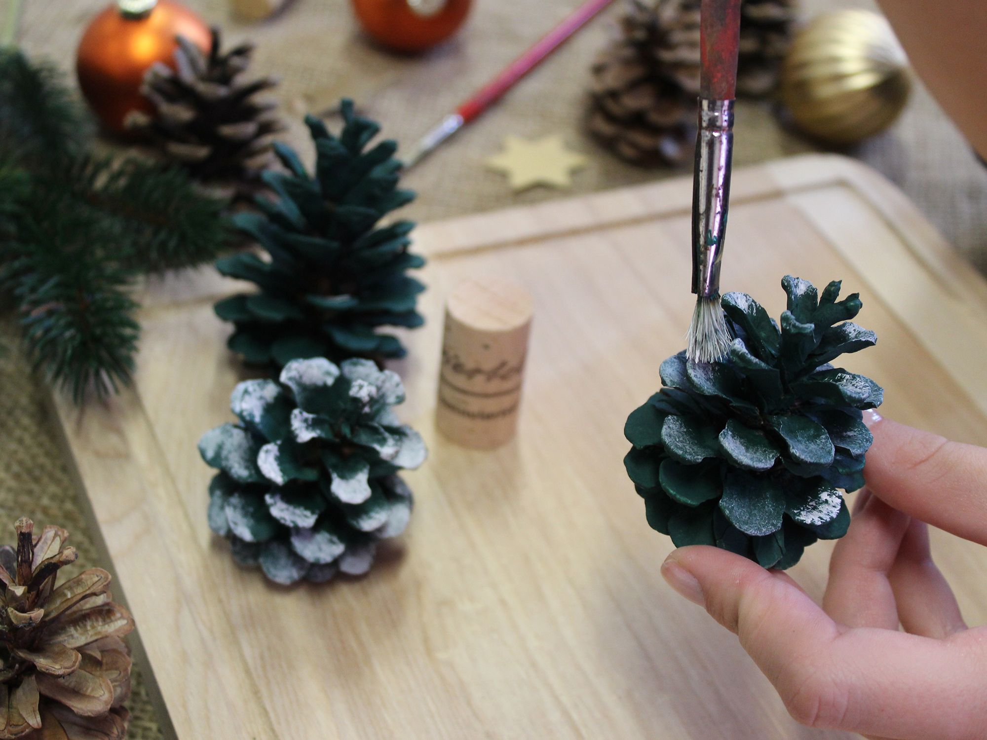 Tannenzapfen werden mit grüner und weißer Farbe bemalt.