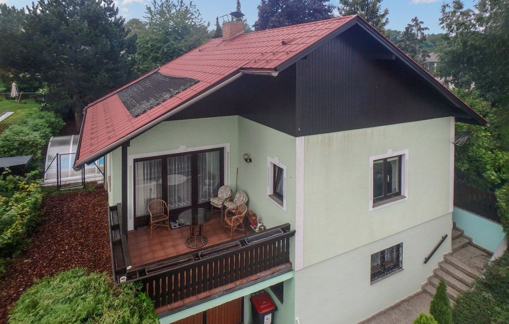 Zweistöckiges Haus mit rotem Dach und Balkon, umgeben von Bäumen.