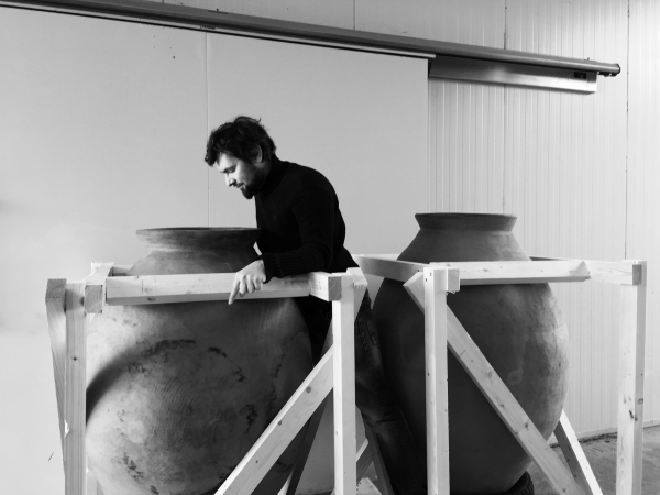 Person next to large clay amphorae in a wine cellar.