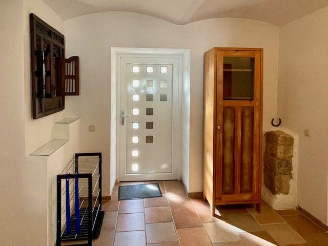 Eingangsbereich mit weißer Tür, Holzschrank und Fliesenboden.