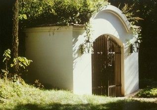 Weißes Mausoleum mit Metalltor im Wald.