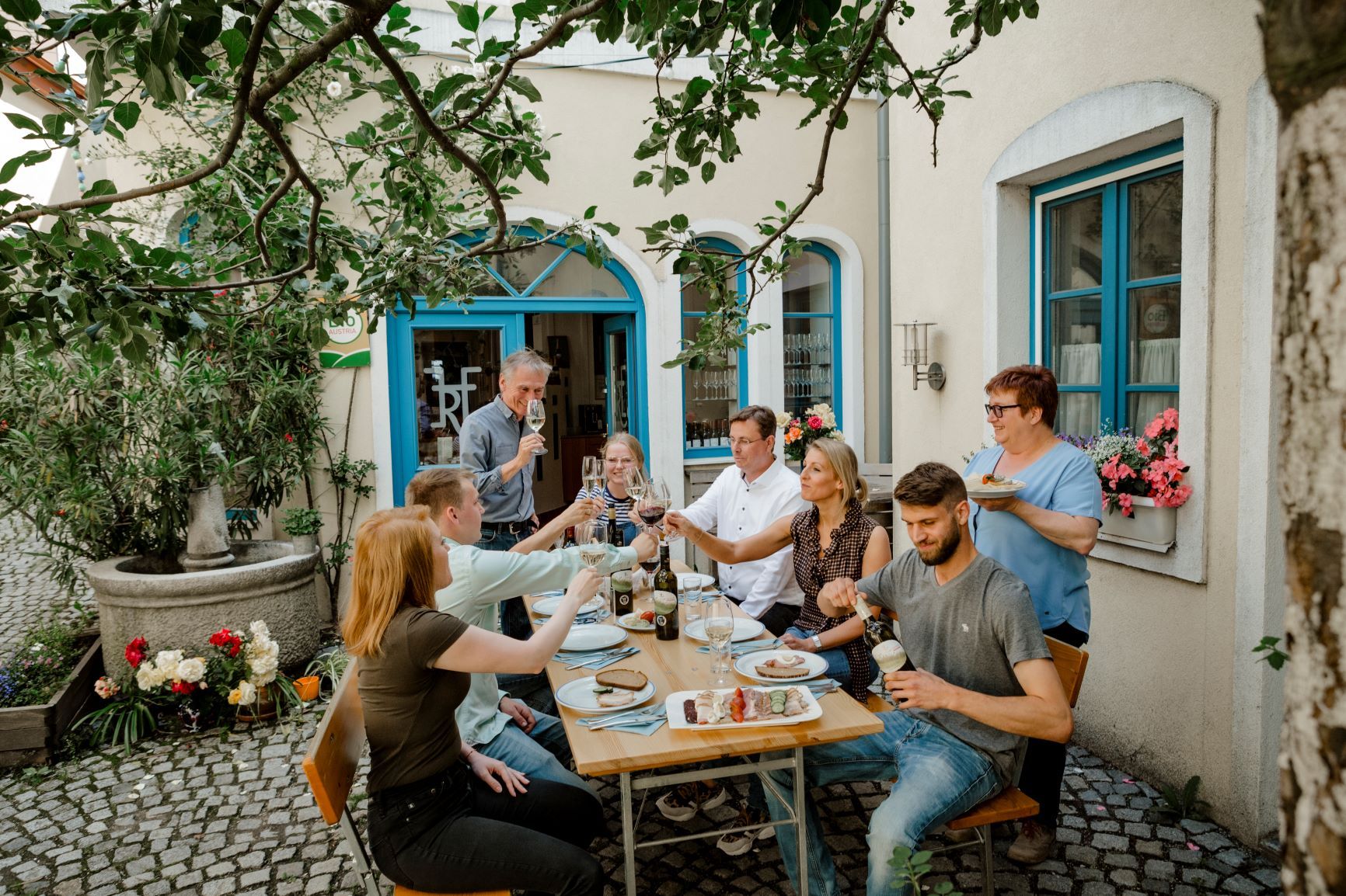 Eine Gruppe von Menschen sitzt an einem Tisch im Freien und stößt mit Getränken an.