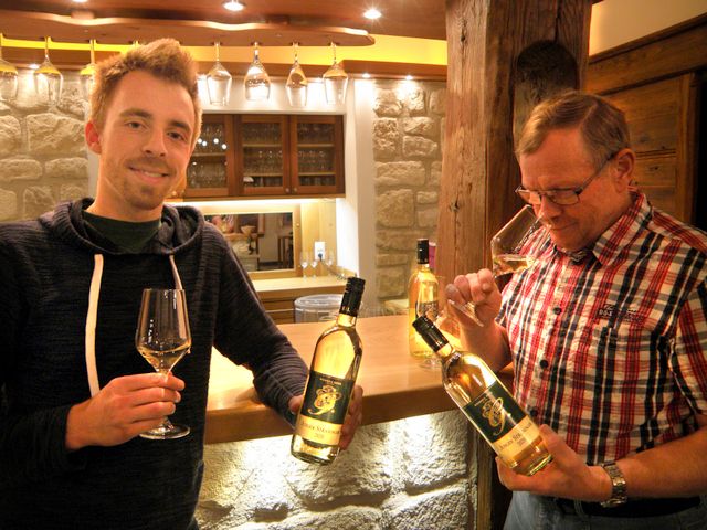Two men in a wine bar holding wine glasses and bottles of wine.