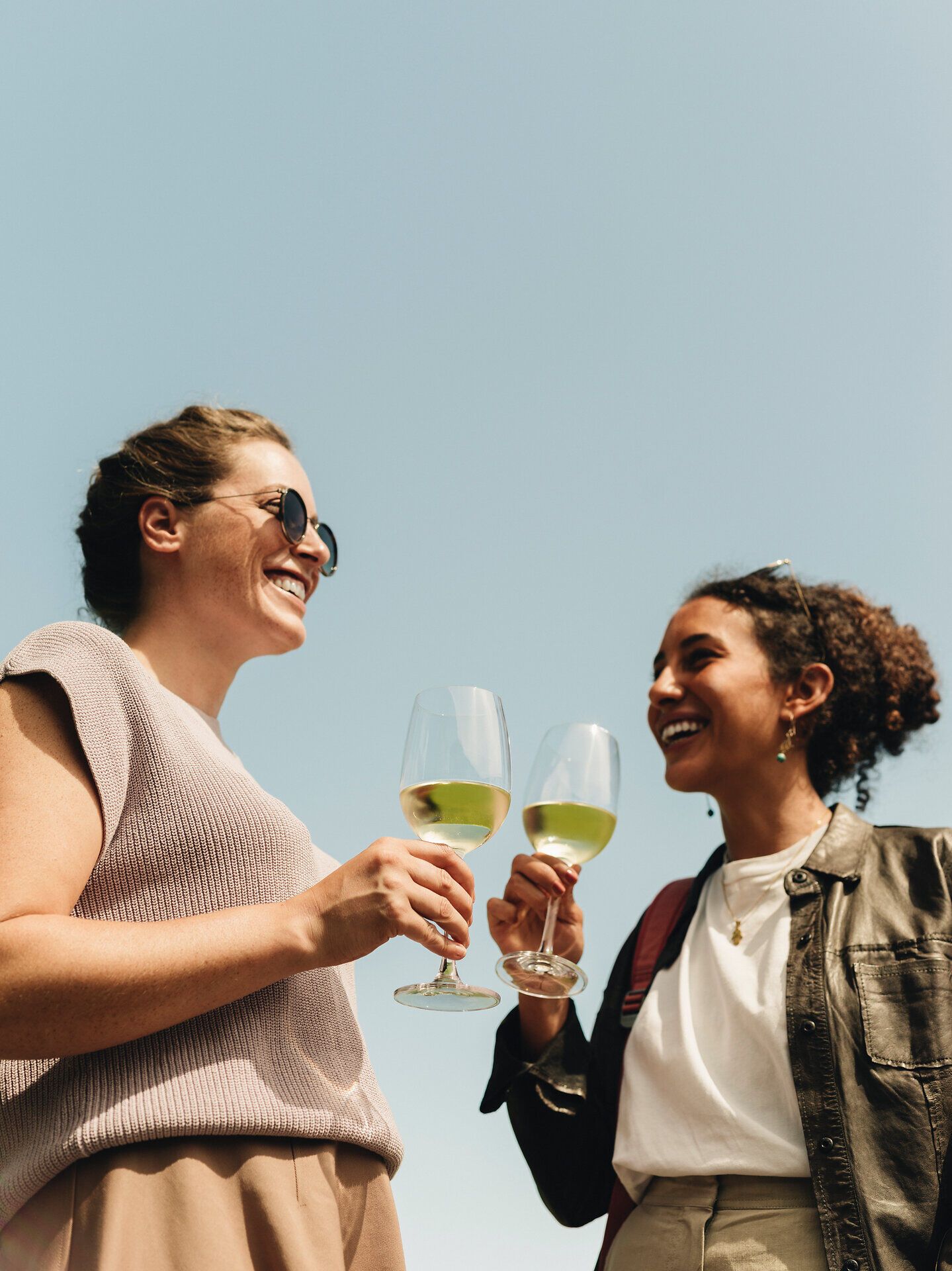 Zwei Freundinnen stoßen mit Gläsern voll erfrischendem Wein an und genießen die strahlende Sonne. Umgeben von sanften Hügeln und üppigen Weinreben, strahlt die Atmosphäre Freude und Entspannung aus. Der Weinherbst lädt dazu ein, die köstlichen Aromen der Region zu entdecken.