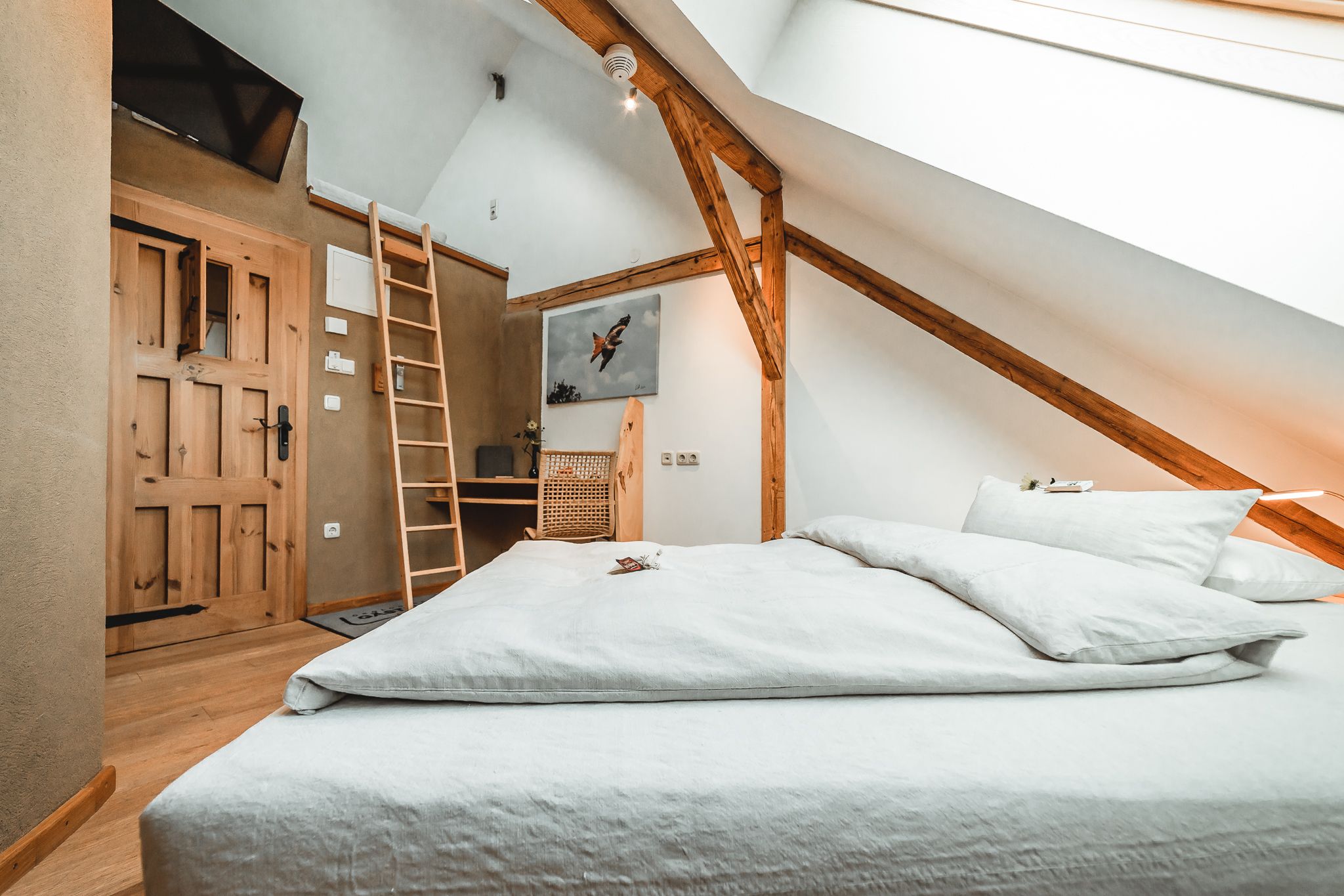 Gemütliches Gästezimmer mit Holzbalken, einem Bett, Leiter zu einem Hochbett und einem Schreibtisch mit Stuhl.