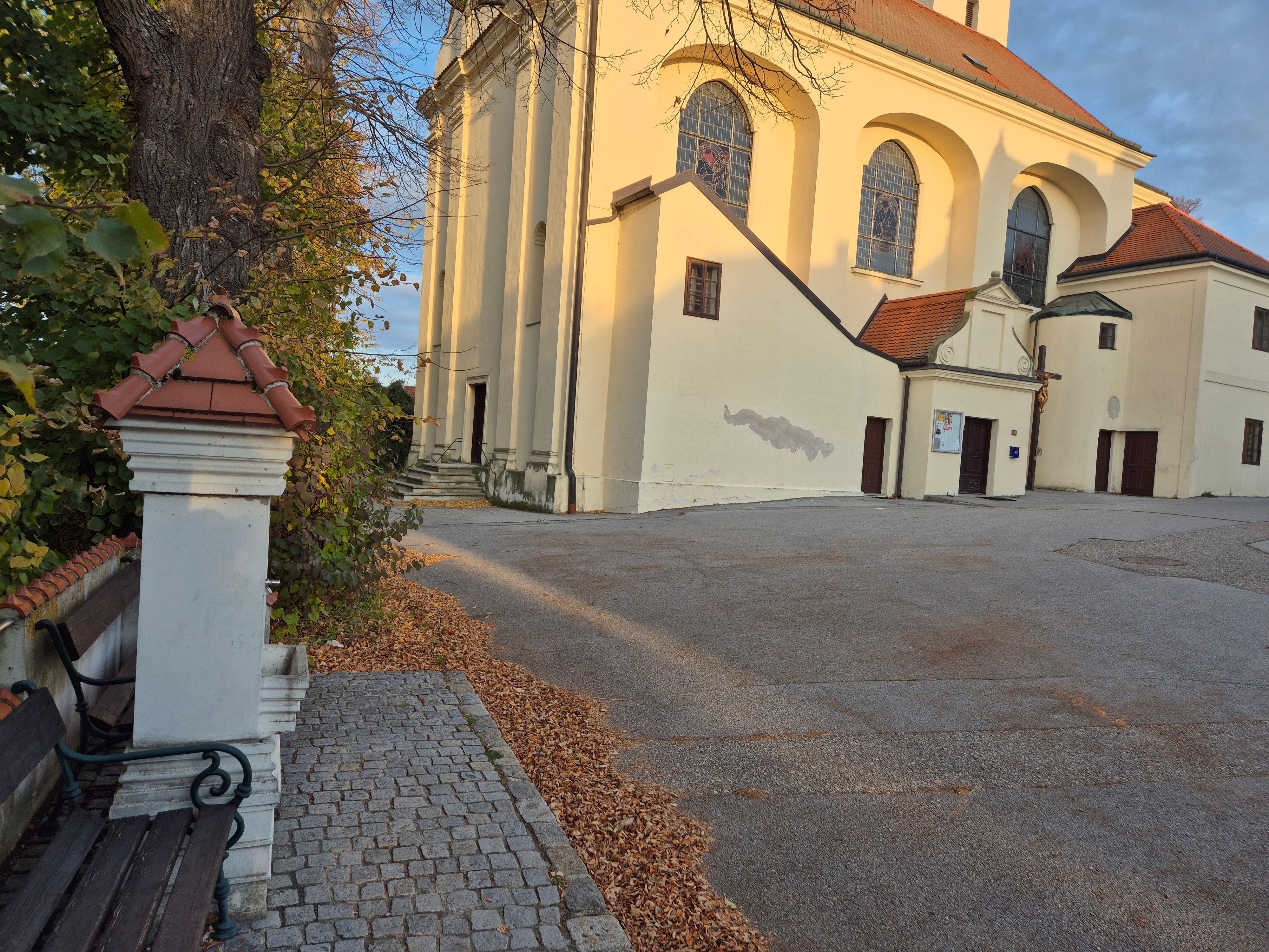 Church with a yellow façade and red roofs, surrounded by autumn leaves and trees.