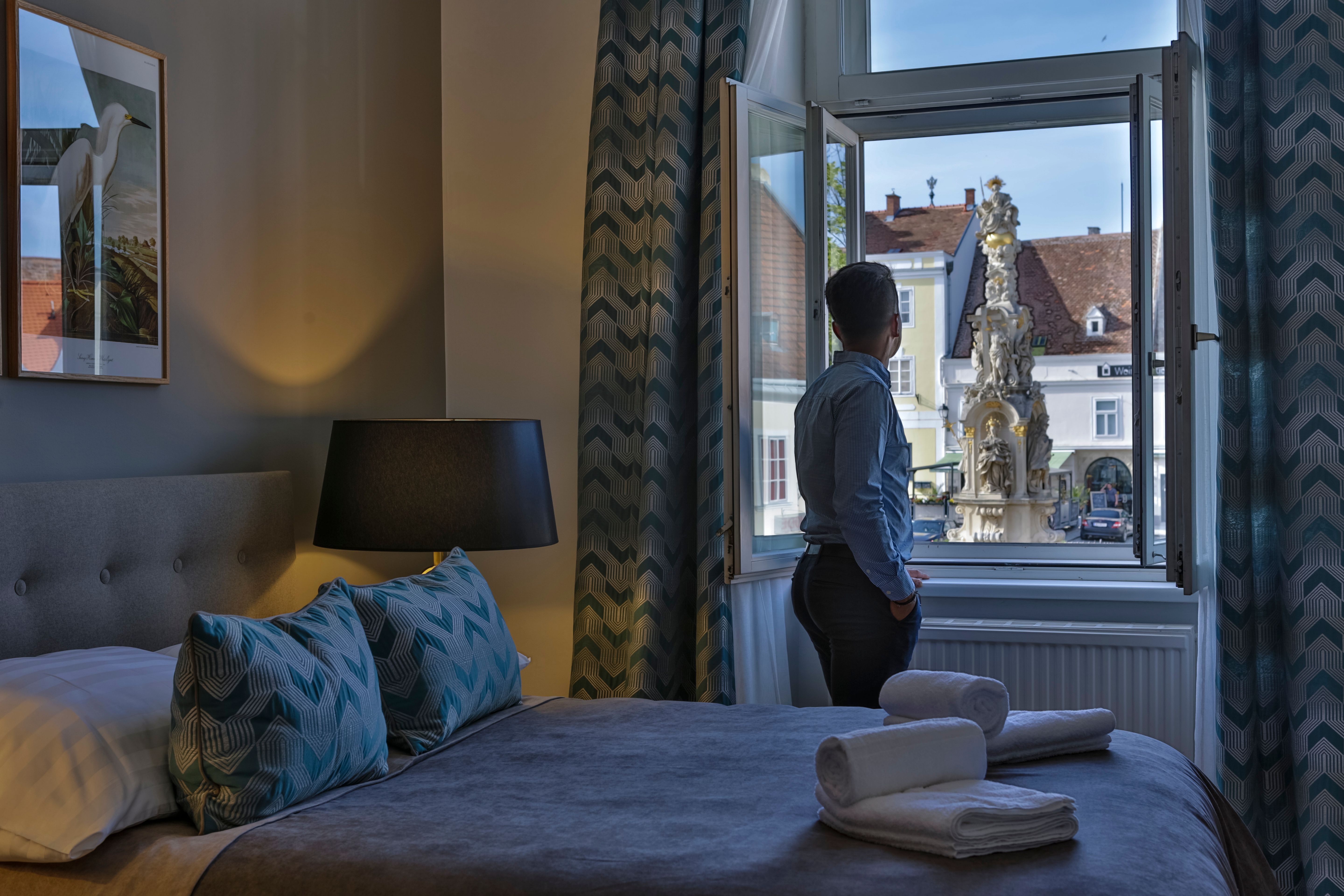 Person steht am Fenster eines Hotelzimmers und blickt auf einen Brunnen draußen.