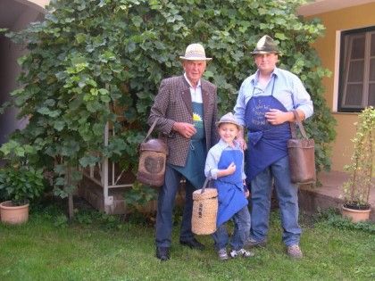 Three generations of men in traditional clothing with baskets in the garden.