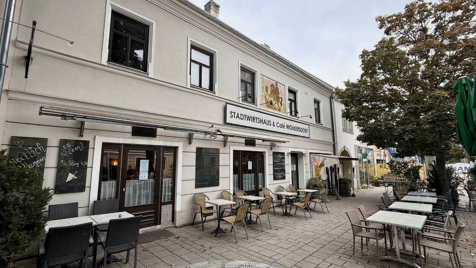 Außenansicht eines Cafés mit Tischen und Stühlen auf dem Gehweg.