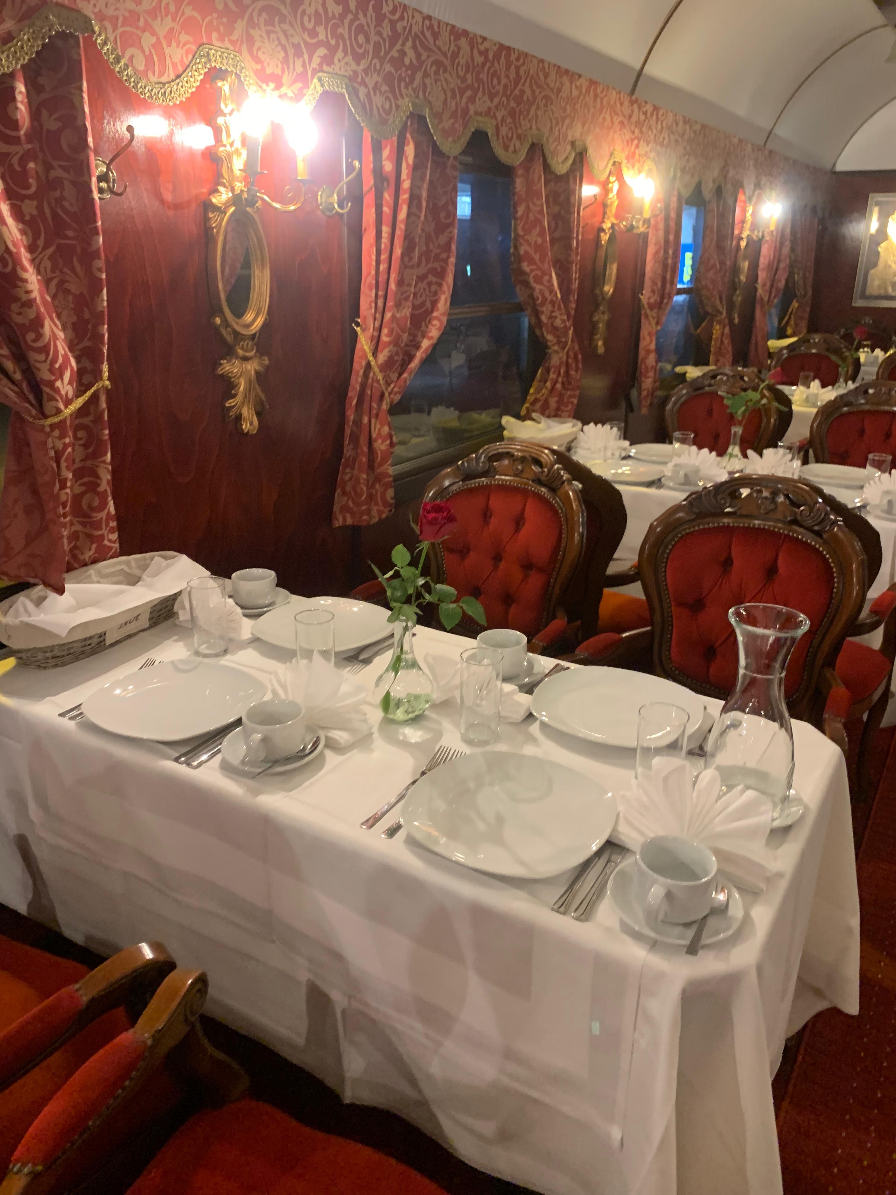 Elegantes Interieur eines Speisewagens mit roten Polstersesseln und gedecktem Tisch.
