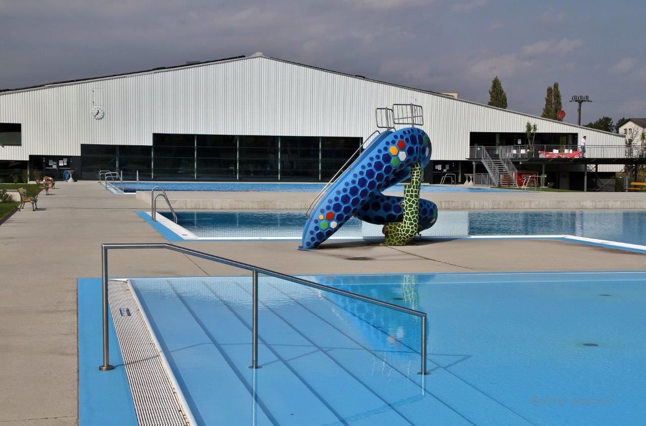 Ein leeres Freibad mit einer bunten Rutsche und einem großen Gebäude im Hintergrund.