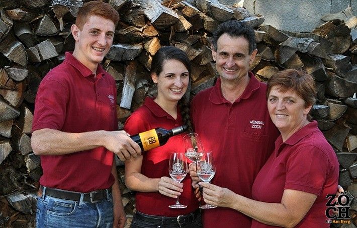 Four people in red shirts clink glasses of wine in front of a pile of logs.