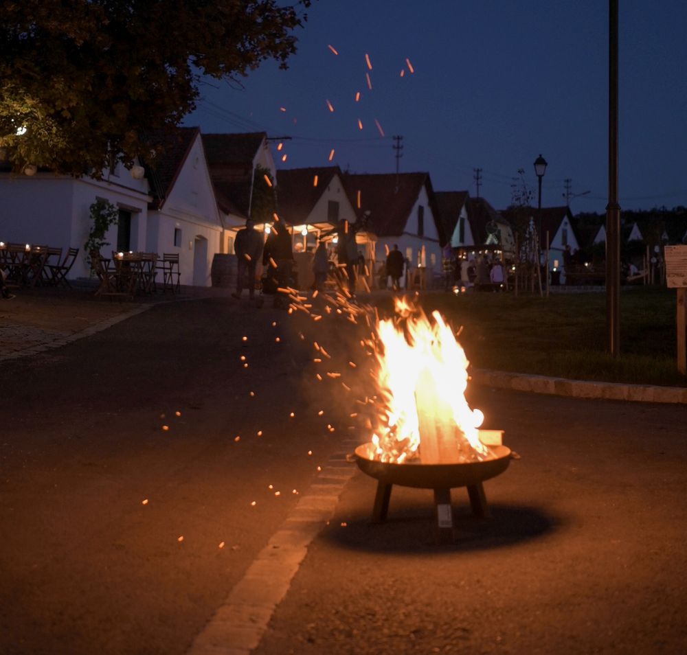 Eine romantische Nacht entfaltet sich unter dem klaren Sternenhimmel, während das sanfte Licht der Flammen die Umgebung in warmen Tönen erleuchtet. Die Atmosphäre ist erfüllt von der Vorfreude auf Wein und Kunst, die hier in der Kellergasse zelebriert werden.